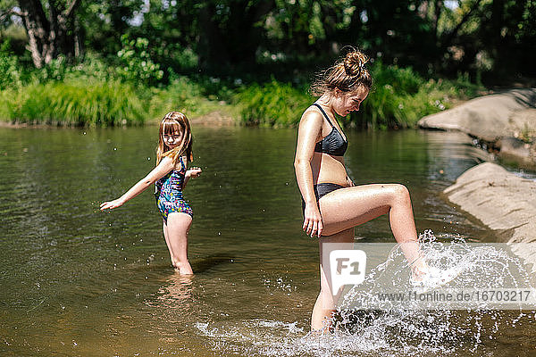Schwestern spielen und planschen an einem sonnigen Tag in einem Fluss