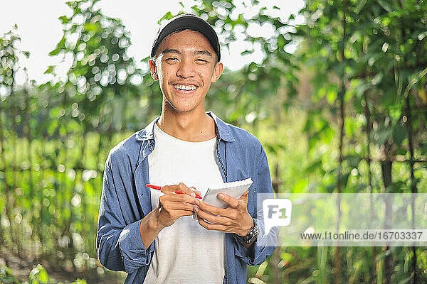 Happy of smiling young Asian farmer male holding the notebook on green garden