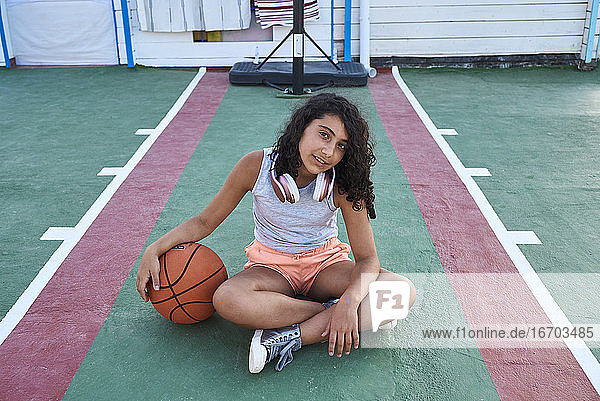 Ein Mädchen sitzt mit einem Basketball vor der Kamera