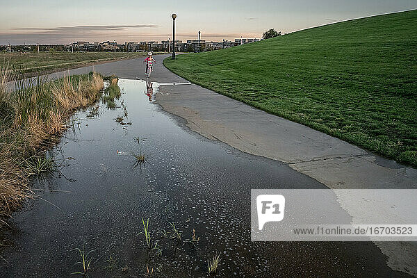 girl rides a bike toward a puddle on the sidewalk in a park