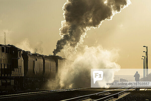 Stark rauchende Dampflok bewegt sich auf dem Gleis in den gelben Sonnenaufgang