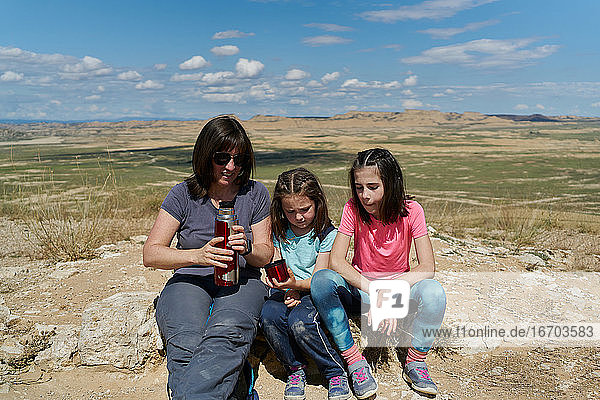 Mutter und zwei Töchter machen eine Pause und trinken Wasser in der Wüste Bardenas Reales in Spanien