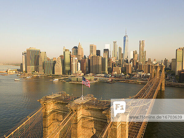 Brookyln Bridge Luftaufnahme mit wehender amerikanischer Flagge und Manhattan Skyline im Hintergrund im Tageslicht
