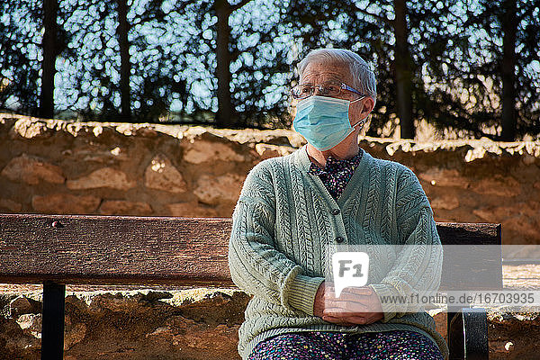 Ältere Frau sitzt mit Maske auf einer Parkbank