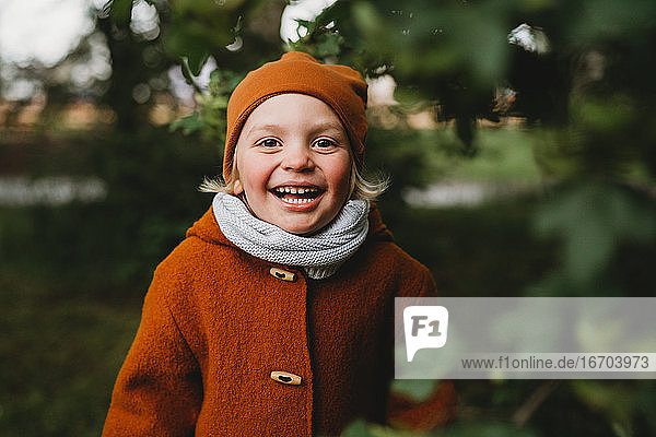 Gut aussehender Junge lächelt im Park zwischen Blättern in Erdtönen