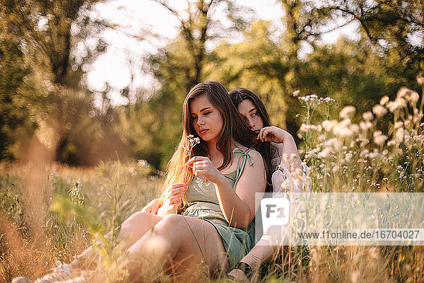 Thoughtful lesbian couple sitting in field of flowers in forest
