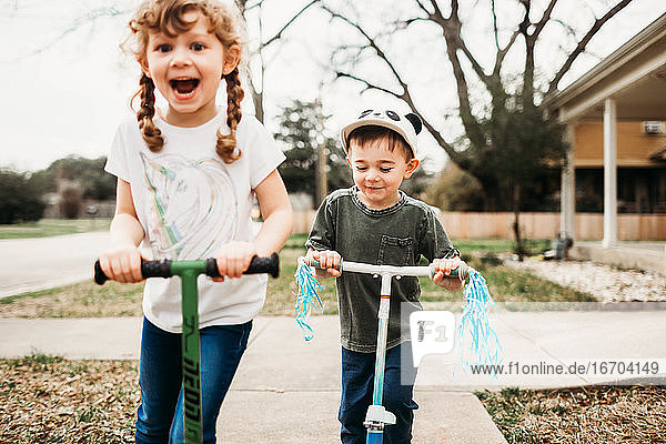 Junge Schwester und Bruder fahren Roller draußen im Vorgarten