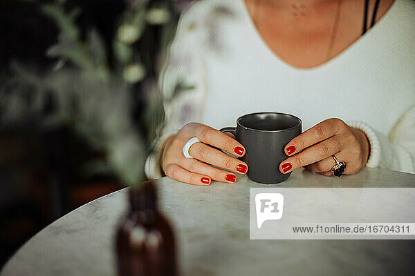 Mittelteil einer Frau  die eine Tasse Kaffee hält  während sie am Tisch sitzt