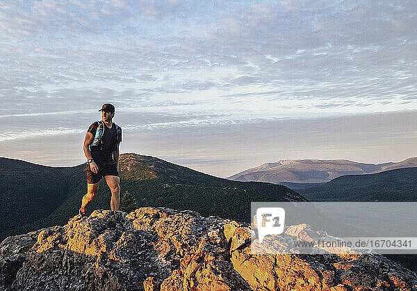 fitter männlicher Wanderer geht bei Sonnenaufgang in den Bergen von Maine einen felsigen Pfad entlang