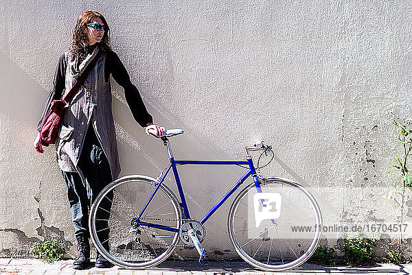 Junge Frau lehnt an einer Stadtmauer mit Vintage-Fahrrad in sonnigen Tag