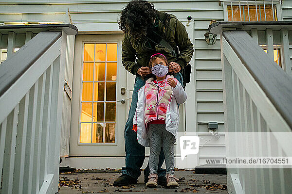 Father securing face mask on daughter before trick or treating COVID