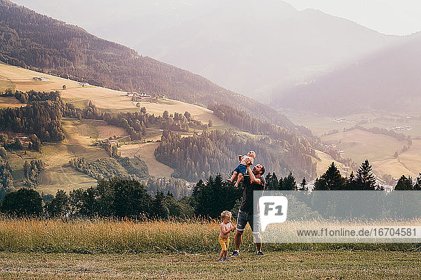 Father throwing baby in the air with mountains in the back in summer