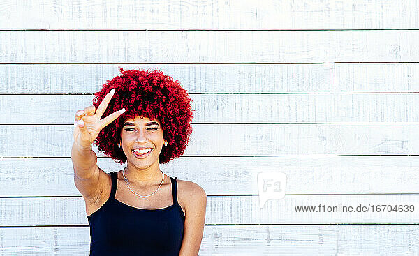 Porträt einer Frau mit rotem Afro  die mit den Fingern das Siegeszeichen zeigt.
