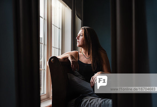 Spiegelreflexion einer hübschen Frau  die in einem dunklen Raum aus dem Fenster schaut.