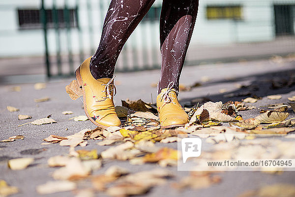Beine einer Frau in gelben Schuhen auf Herbstblättern