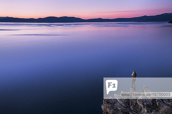 Frau betrachtet die Aussicht  während sie bei Sonnenuntergang auf einer Felsformation am Lake Tahoe steht