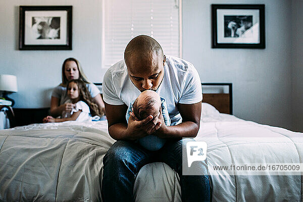 Center portrait of dad kissing newborn baby on bed