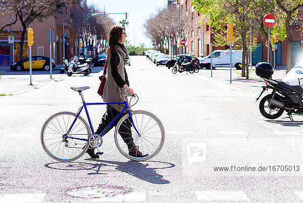 Young smiling woman walking on a city street with bicycle