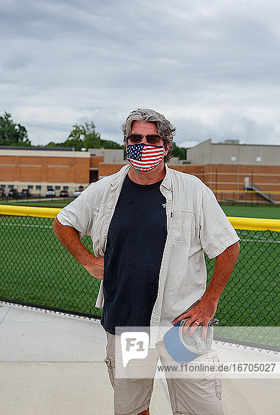 Obere Hälfte eines Mannes mit einer Maske mit amerikanischer Flagge vor einer High School