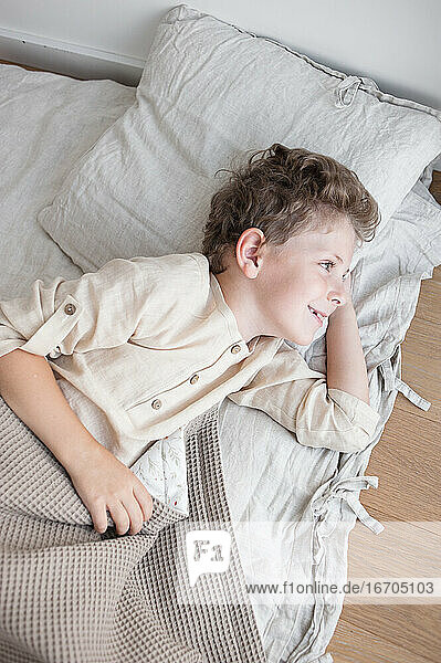 Ein Junge in Hauskleidung liegt nach dem Aufwachen freudig in einem natürlichen Bettzeug.