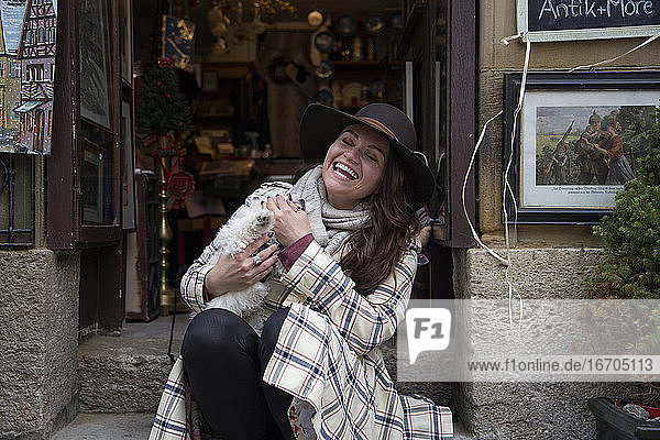 Eine Frau lacht wild  während sie einen kleinen weißen Welpen auf einer Türschwelle hält