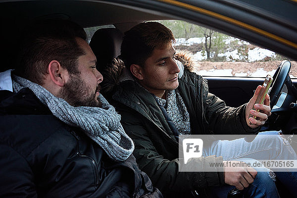 Zwei junge Männer schauen auf ein Telefon in einem Auto. Konzept der Routenfindung