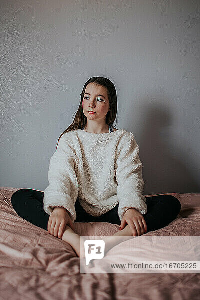 vertikales Porträt eines Mädchens auf dem Bett sitzend und wegschauend