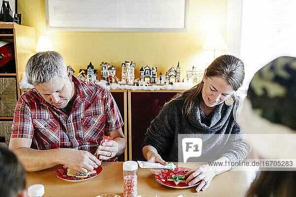 Vater und Mutter dekorieren während der Ferienzeit Zuckerplätzchen zu Hause