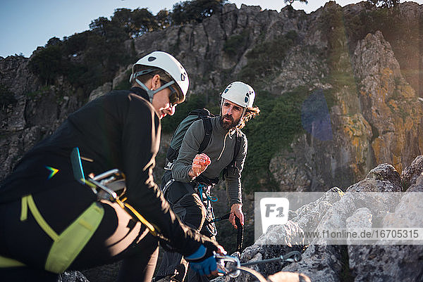 Concept: adventure. Man and woman with helmet  harness. Explaining climbing techniques. Solar luminous flare.Via ferrata in the mountains.