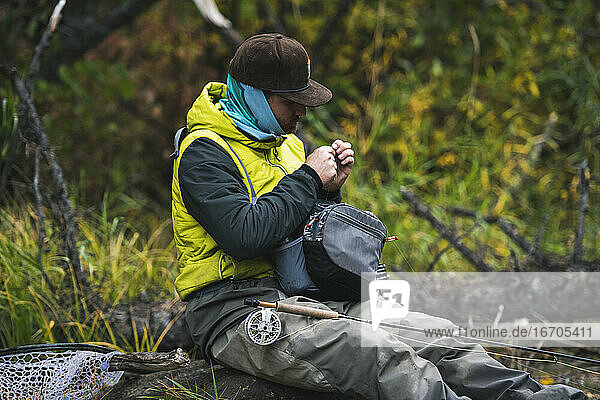 Mann sitzend beim Fliegenfischen im Wald