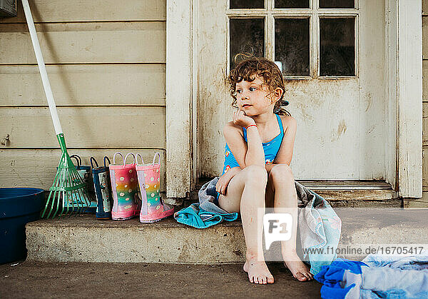 Junges Mädchen sitzt auf der hinteren Veranda und trägt Badeanzug und Handtuch