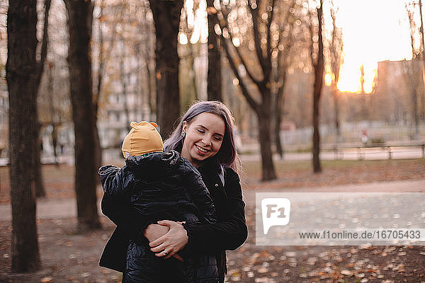 Glückliche junge Mutter mit Baby Sohn im Park im Herbst bei Sonnenuntergang