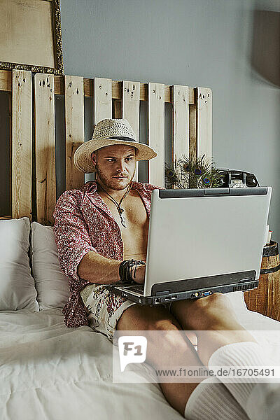 ein Mann arbeitet mit seinem Laptop in einem Hotelbett.