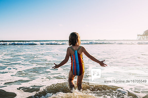 behind shot of young girl running into ocean