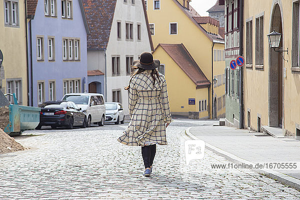 Eine Frau in einem langen Mantel geht durch die Straßen einer mittelalterlichen Stadt.