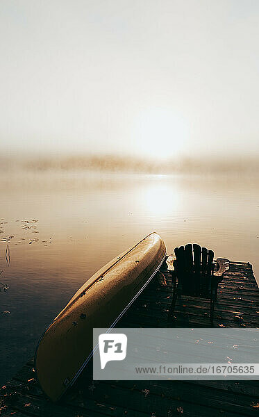 Leerer Steg mit umgestürztem Kanu an einem nebligen Morgen auf einem ruhigen See.