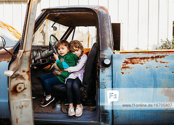 Junger Bruder und junge Schwester sitzen und umarmen sich in einem alten Lastwagen
