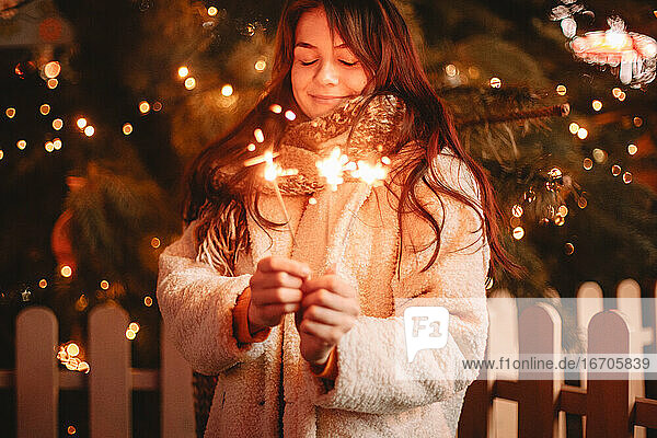 Glückliches Teenager-Mädchen mit Wunderkerzen vor einem Weihnachtsbaum
