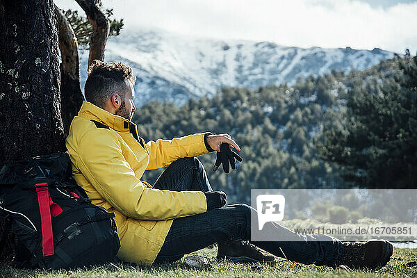 Young man with yellow jacket and backpack sitting on the mountain.
