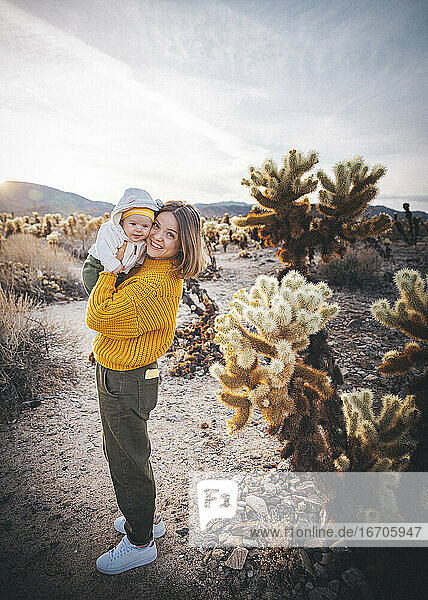 Eine Frau mit einem Baby steht in der Nähe eines Kaktus in der Wüste