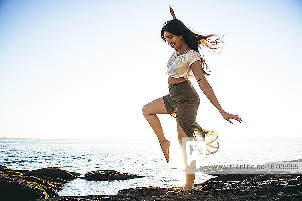 Junge Latina Frau tanzt am Meer zur goldenen Stunde im Sommer