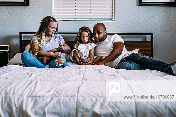 Eine Familie  die mit ihrem neugeborenen Baby auf dem Bett kuschelt
