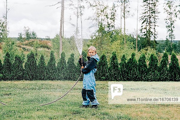 boy standing with a hose spraying water at home in the yard