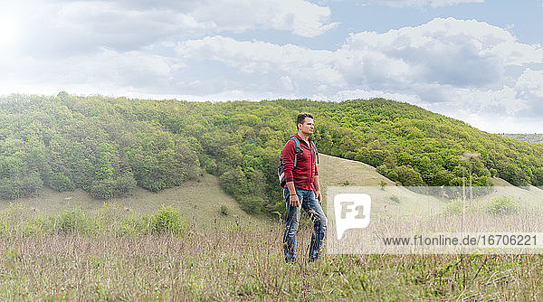 Erwachsener Mann mit Rucksack klettert auf die grünen Hügel und bewundert die s