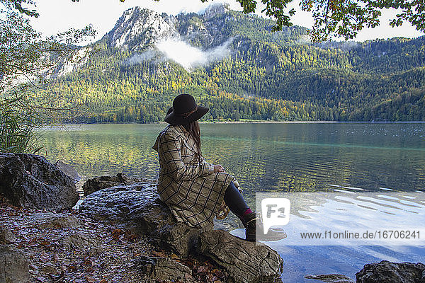 Eine Frau sitzt auf einem Felsen an einem Alpensee in Deutschland