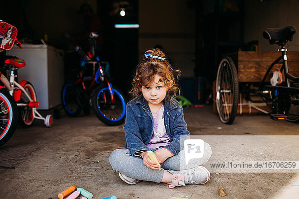 Junges Mädchen sitzt in der Garage und malt mit Kreide im Frühling