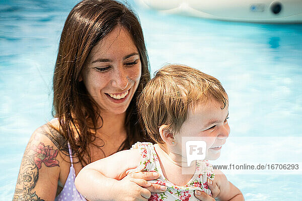 Frau in der Mitte des Pools hält ein kleines Mädchen  das lächelnd ist