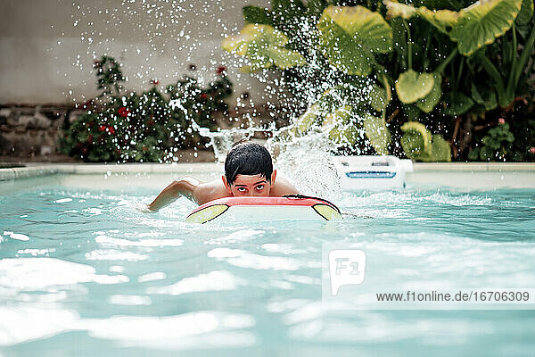 Handsome and dark-haired boy playing with a body surf board in the pool