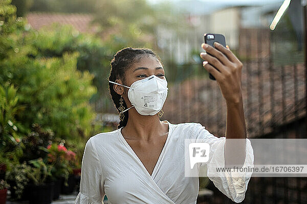 Junge schwarze Frau mit Gesichtsmaske  die ein Smartphone benutzt