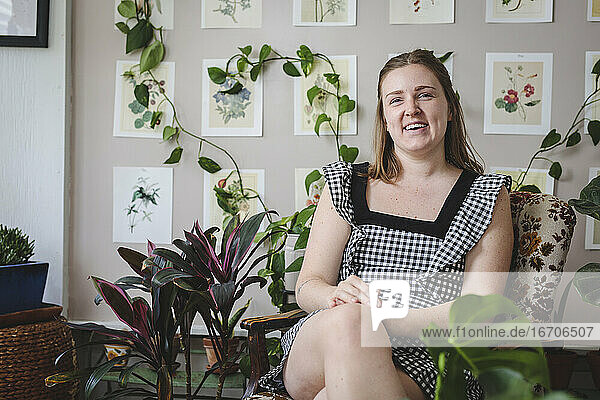 Stilvolle junge Frau lächelt  während sie auf einem Stuhl mit Pflanzen sitzt
